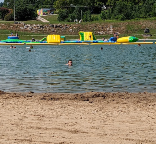 A sandy beach with people swimming in a lake, featuring colorful inflatable structures in the background.