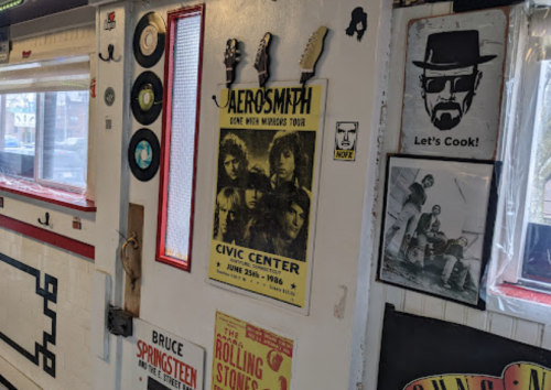 A wall decorated with music posters, vinyl records, and framed photos, featuring Aerosmith and other iconic bands.