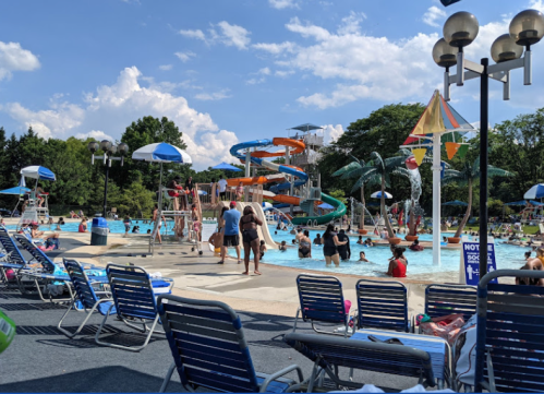A busy water park with a large pool, water slides, and people enjoying the sun on lounge chairs.