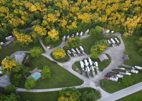 Aerial view of a campground with RVs, a pool, and surrounded by trees with autumn foliage.