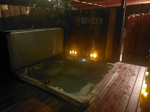 A cozy outdoor hot tub surrounded by candles and wooden fencing, with a sign that says "RELAX."