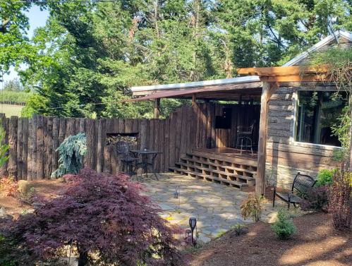A cozy outdoor patio with stone flooring, wooden fencing, and a small table set among lush greenery.