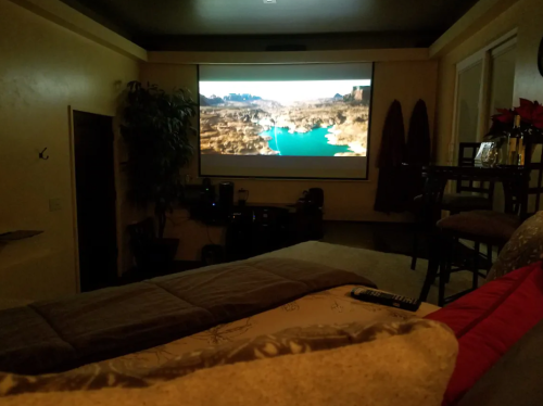 A cozy room with a large screen displaying a scenic landscape, featuring a lake and mountains, with a bed in the foreground.