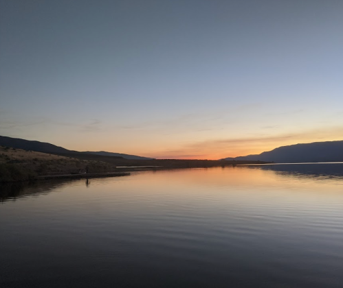 A serene lake at sunset, with mountains in the background and calm water reflecting the colorful sky.