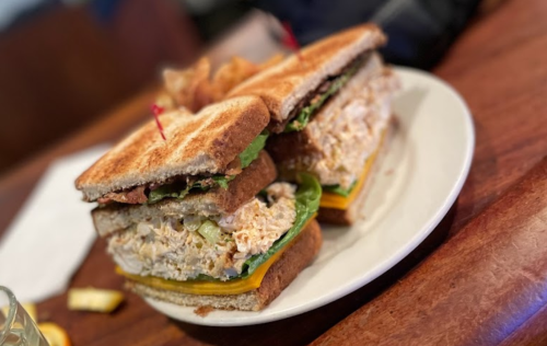 A stacked sandwich with toasted bread, filled with chicken salad, lettuce, and cheese, served on a plate.