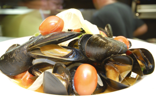 A close-up of a dish featuring mussels, cherry tomatoes, and herbs in a savory broth.