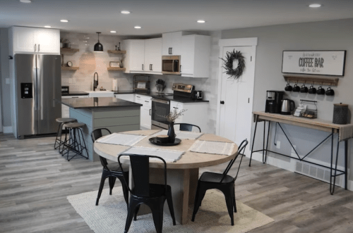 Modern kitchen with a round wooden table, black chairs, stainless steel appliances, and a cozy coffee bar setup.