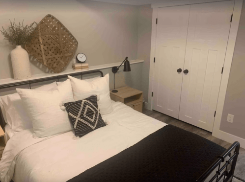 Cozy bedroom featuring a bed with white linens, decorative pillows, a nightstand, and a closet in a neutral-toned room.
