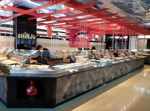 A spacious buffet restaurant with a variety of food stations and modern decor, featuring hanging lights and colorful designs.
