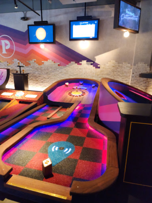 A colorful mini-golf course with illuminated pathways and screens in a modern entertainment space.