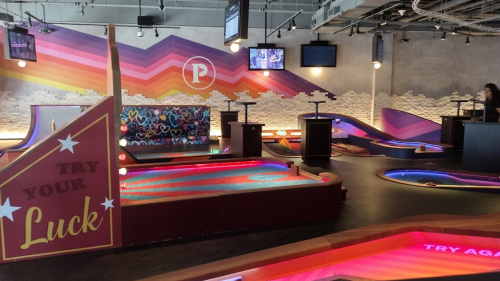 Colorful mini-golf course with vibrant walls, illuminated holes, and a "Try Your Luck" sign in a lively indoor setting.