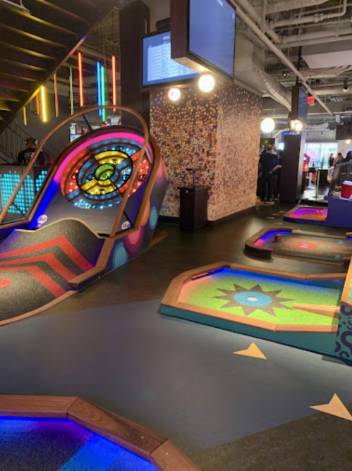 Colorful mini-golf course with illuminated holes and a vibrant, playful design in a lively indoor setting.