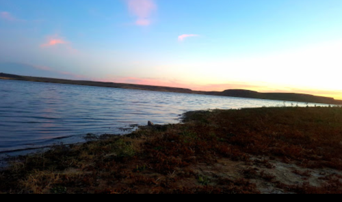 A serene lakeside view at sunset, with calm water and a colorful sky reflecting soft hues.