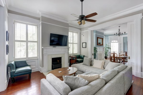 A spacious living room with a large sectional sofa, fireplace, TV, and dining area in a bright, airy setting.