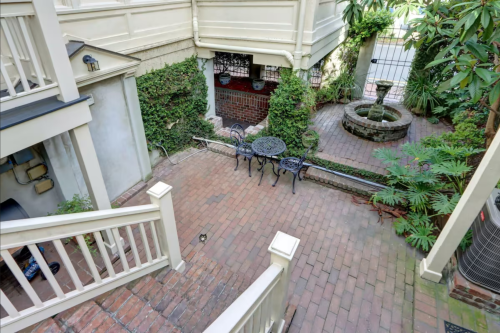 A brick patio with a small table and chairs, surrounded by greenery and a fountain, viewed from above.