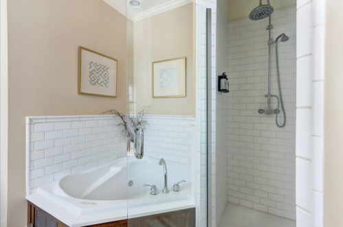 A modern bathroom featuring a corner bathtub and a glass-enclosed shower with white tile and decorative wall art.