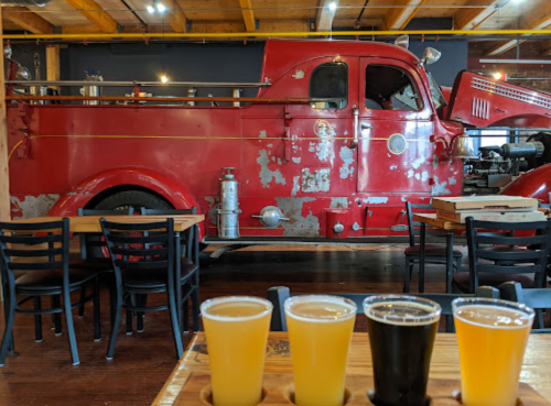 A vintage red fire truck is displayed in a restaurant, with a flight of four craft beers in the foreground.