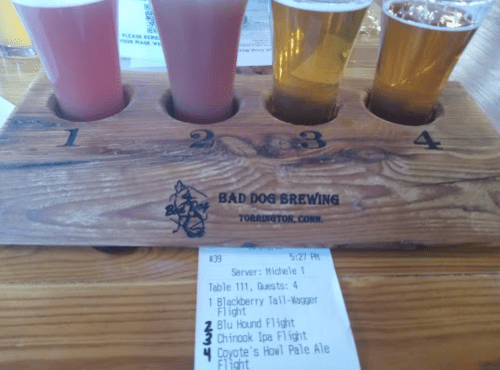 A wooden flight holder with four beer samples and a receipt from Bad Dog Brewing in Torrington, Connecticut.