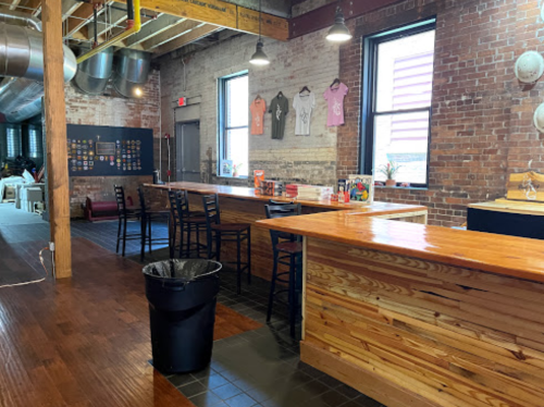 A spacious interior with wooden counters, bar stools, and brick walls, featuring merchandise on display.
