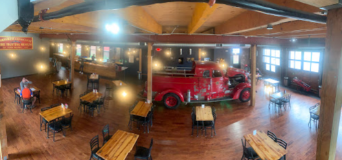 A spacious restaurant interior featuring wooden tables, a vintage red truck, and warm lighting.