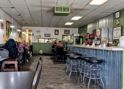 A cozy diner interior with green walls, bar stools, and patrons enjoying their meals at tables and the counter.