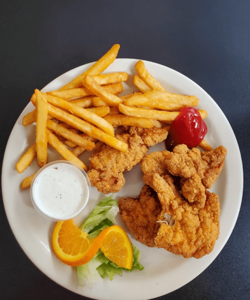 A plate of fried chicken strips, French fries, a side of ranch dressing, lettuce, and orange slices with ketchup.