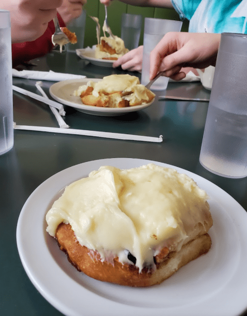 A close-up of a plate with a dessert topped with creamy frosting, surrounded by hands and glasses of water.