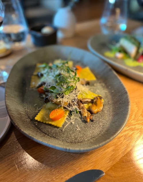 A plate of ravioli topped with vegetables and herbs, served on a textured gray dish.