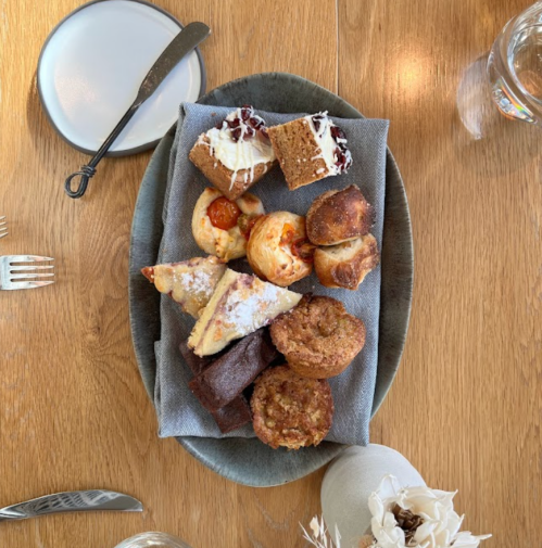 A platter of assorted pastries and baked goods on a gray cloth, set on a wooden table.