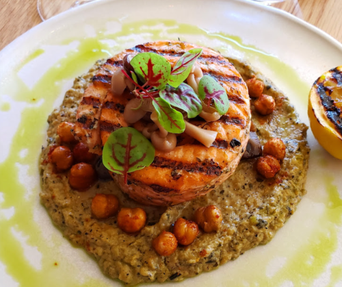 Grilled salmon atop a creamy chickpea puree, garnished with greens and served with roasted lemon halves.