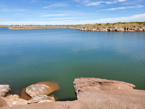A serene body of water surrounded by rocky shores and lush greenery under a clear blue sky.