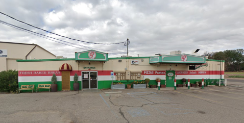 A colorful restaurant exterior with a sign, featuring a green and white facade, plants, and a parking area.