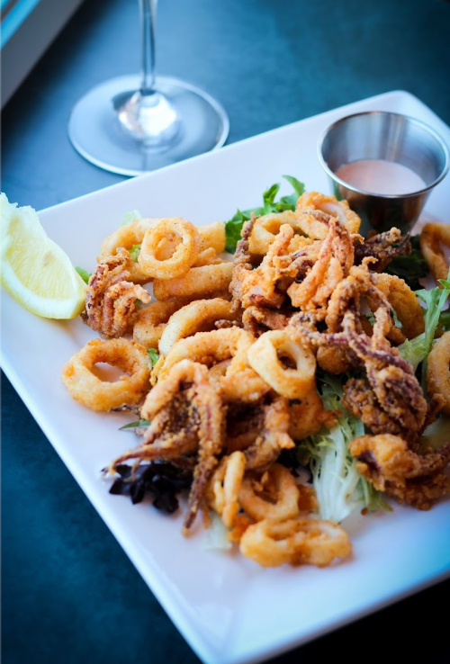 A plate of crispy fried calamari served with a lemon wedge and dipping sauce, garnished with greens.