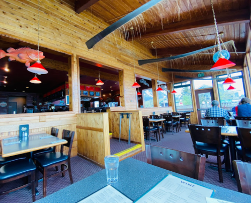 Interior of a cozy restaurant with wooden decor, red pendant lights, and a view of diners at tables.