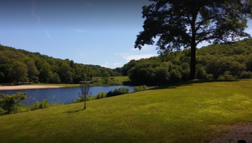 A serene landscape featuring a lake surrounded by lush green hills and a clear blue sky.