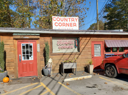 Exterior of Country Corner Kitchen, featuring a wooden facade, red doors, and a sign against a clear blue sky.