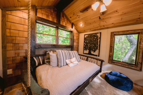 Cozy interior of a cabin with a daybed, wooden walls, and large windows overlooking greenery.