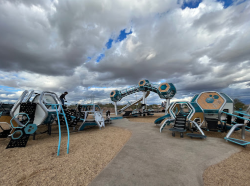 A modern playground with unique climbing structures and slides, set against a cloudy sky.