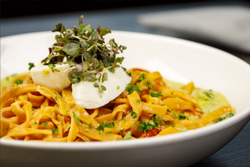 A bowl of fettuccine pasta topped with a poached egg and fresh herbs, garnished with microgreens.