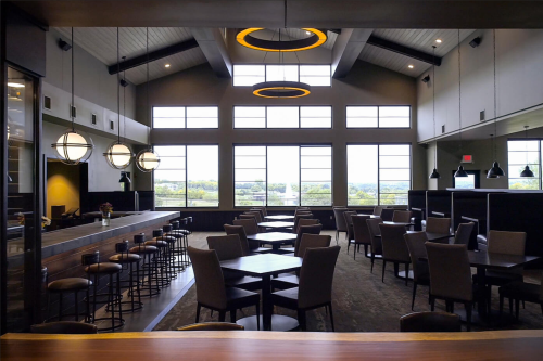 Modern restaurant interior with high ceilings, large windows, and a mix of tables and bar seating.
