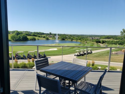 View from a balcony overlooking a golf course, pond, and parked golf carts on a sunny day.