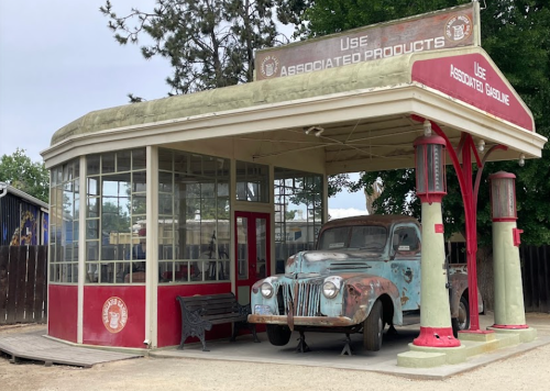 Vintage gas station with a classic car, featuring red and green colors and large windows.