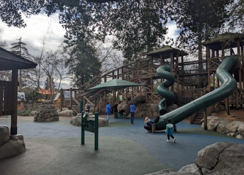 A playground with wooden structures, slides, and children playing on a cloudy day.