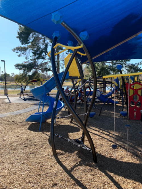 A playground structure with twisting poles, blue slides, and a shaded area, surrounded by wood chips and trees.