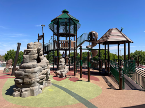 Playground with climbing structures, a slide, and rock formations under a clear blue sky.