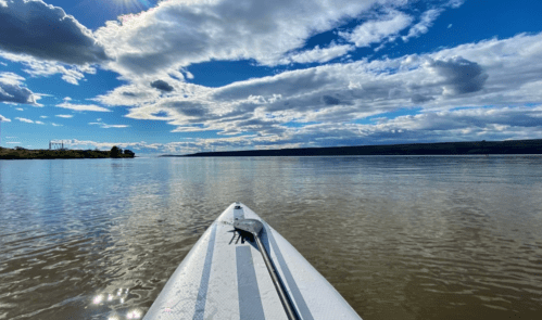 A paddleboard on calm water, with a scenic view of clouds and blue sky reflected in the lake.