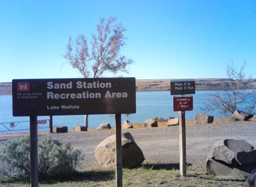 Sign for Sand Station Recreation Area at Lake Wallula, with a reminder to pack out what you pack in. Scenic water view.