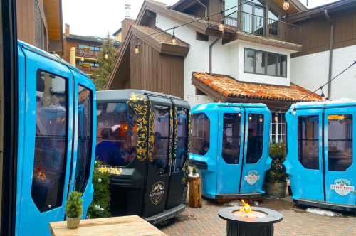 Colorful outdoor dining pods with a fire pit in a cozy courtyard setting, surrounded by rustic buildings and greenery.
