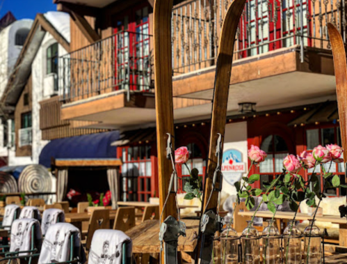 Ski equipment in front of a cozy mountain lodge with flowers on tables and a sunny outdoor seating area.