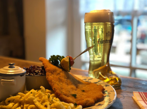 A plate with breaded fish, pasta, and red cabbage, alongside a large beer in a boot-shaped glass.